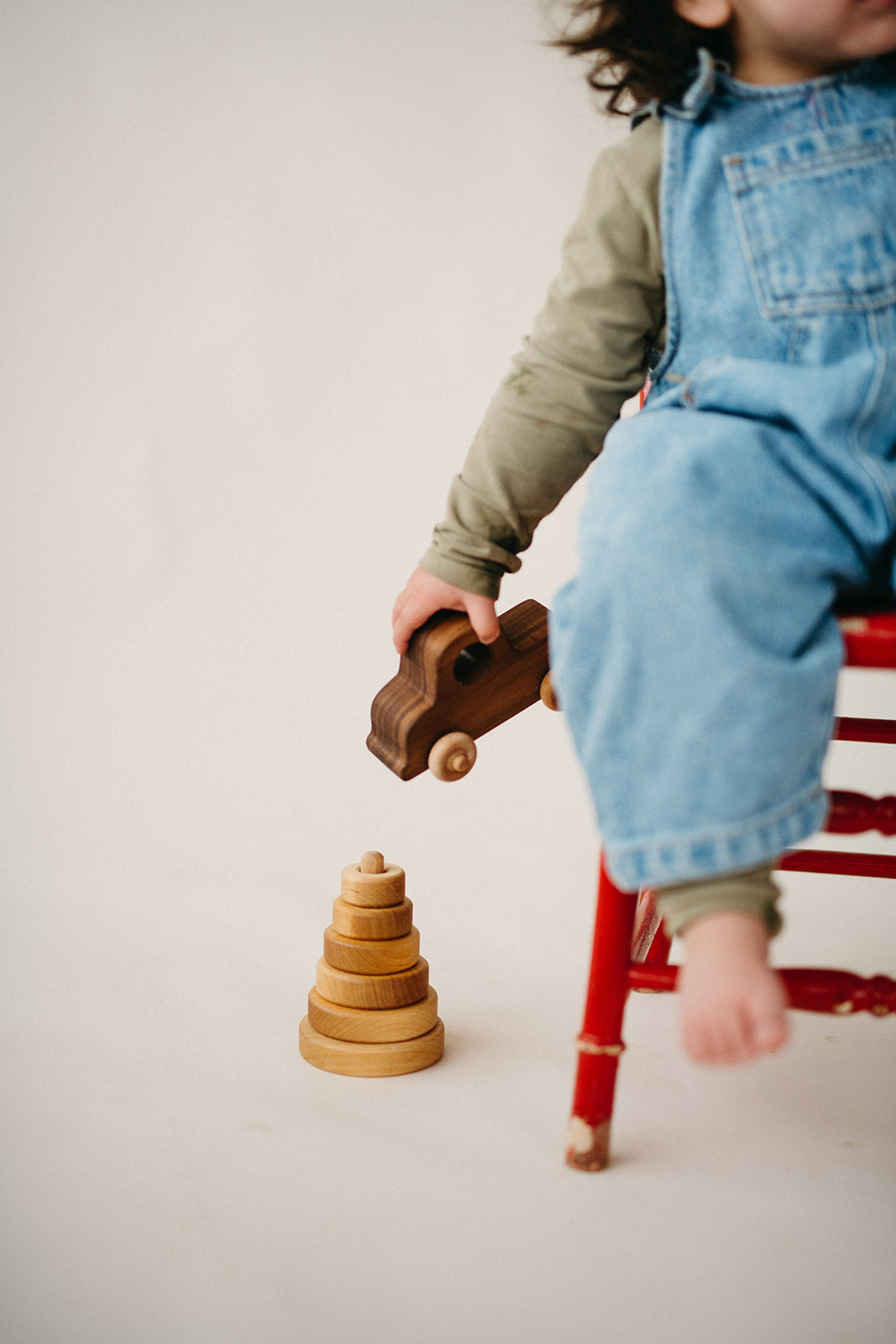 Toddler holding a wooden toy car on a red stool
